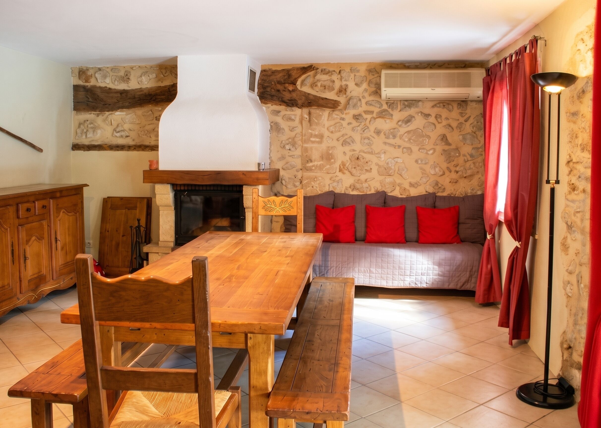 Ein Zimmer mit einem Holzesstisch, Stühlen, einer Couch mit roten Kissen, einem Kamin und einer Steinwand.