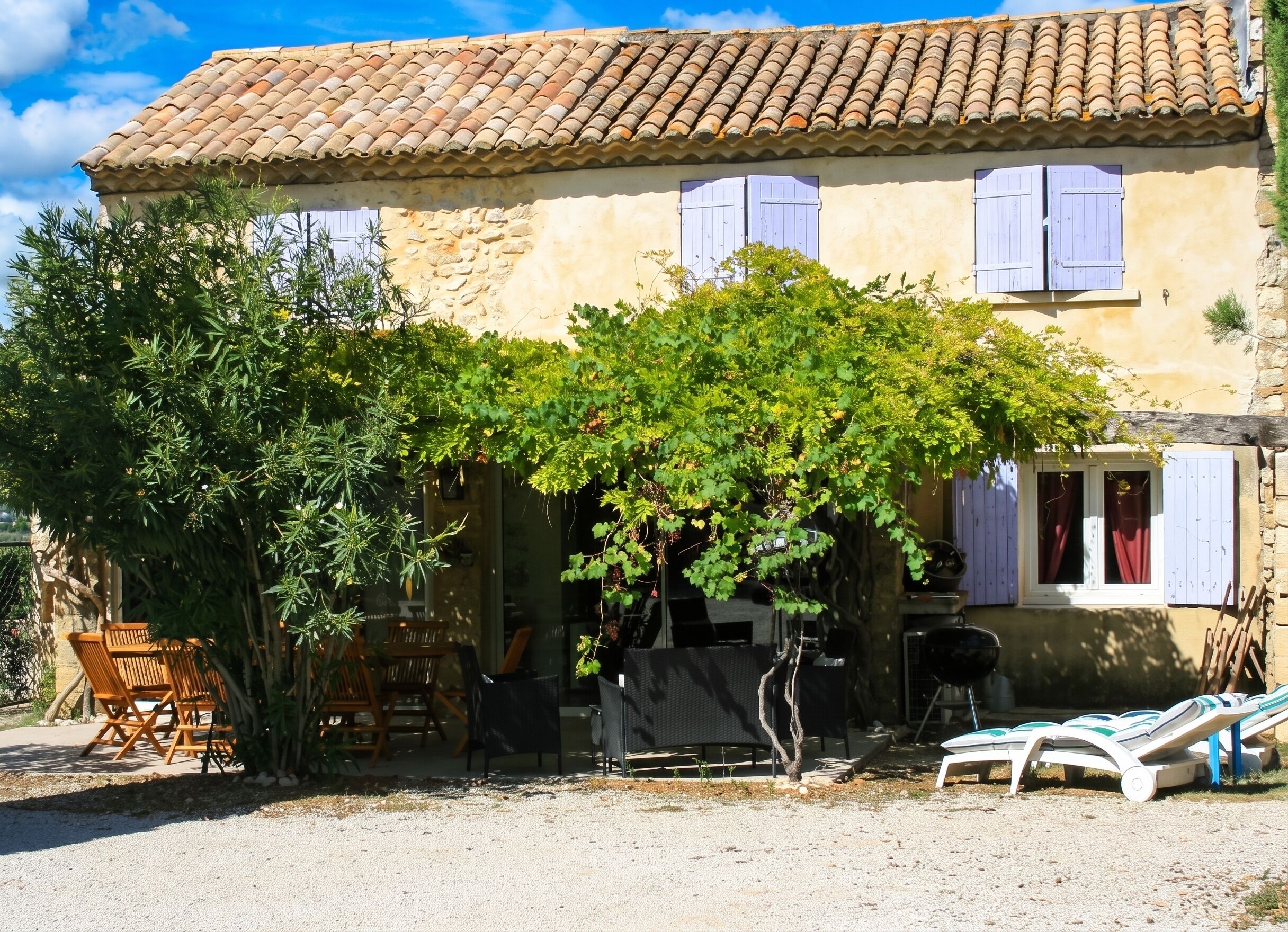 A rustic stone building with a tiled roof, wooden furniture, and a tree in the foreground.