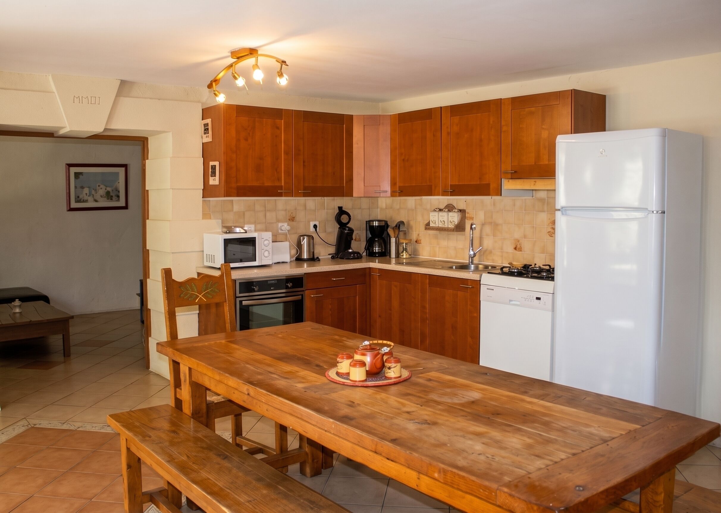 Una cocina con armarios de madera, un refrigerador blanco, un microondas, una estufa y una mesa de comedor con bancos.