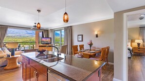 Eine moderne Küche mit einer großen Kochinsel, einem Essbereich mit Holzkästen, einem Fernseher und einer schönen Aussicht.