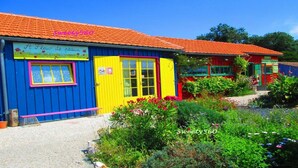 Un edificio colorido con fachada azul y puertas amarillas, rodeado de abundante follaje y un cielo azul despejado.