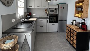 Una cocina moderna con armarios grises, un reloj de pared grande, una lámpara colgante y un aparador de madera.