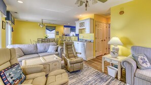 A living room with a sofa, armchairs, a ceiling fan, and a kitchen area with cabinets and a dining table. - Oceanfront Beach House with Stunning Views & Direct Access (North Topsail Beach)