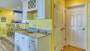 A kitchen with white cabinets, a granite countertop, and a small island. There are two white doors and a yellow wall. - Oceanfront Beach House with Stunning Views & Direct Access (North Topsail Beach)