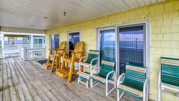 A covered porch with wooden chairs and a bench, a railing, and a view through the glass doors. - Oceanfront Beach House with Stunning Views & Direct Access (North Topsail Beach)