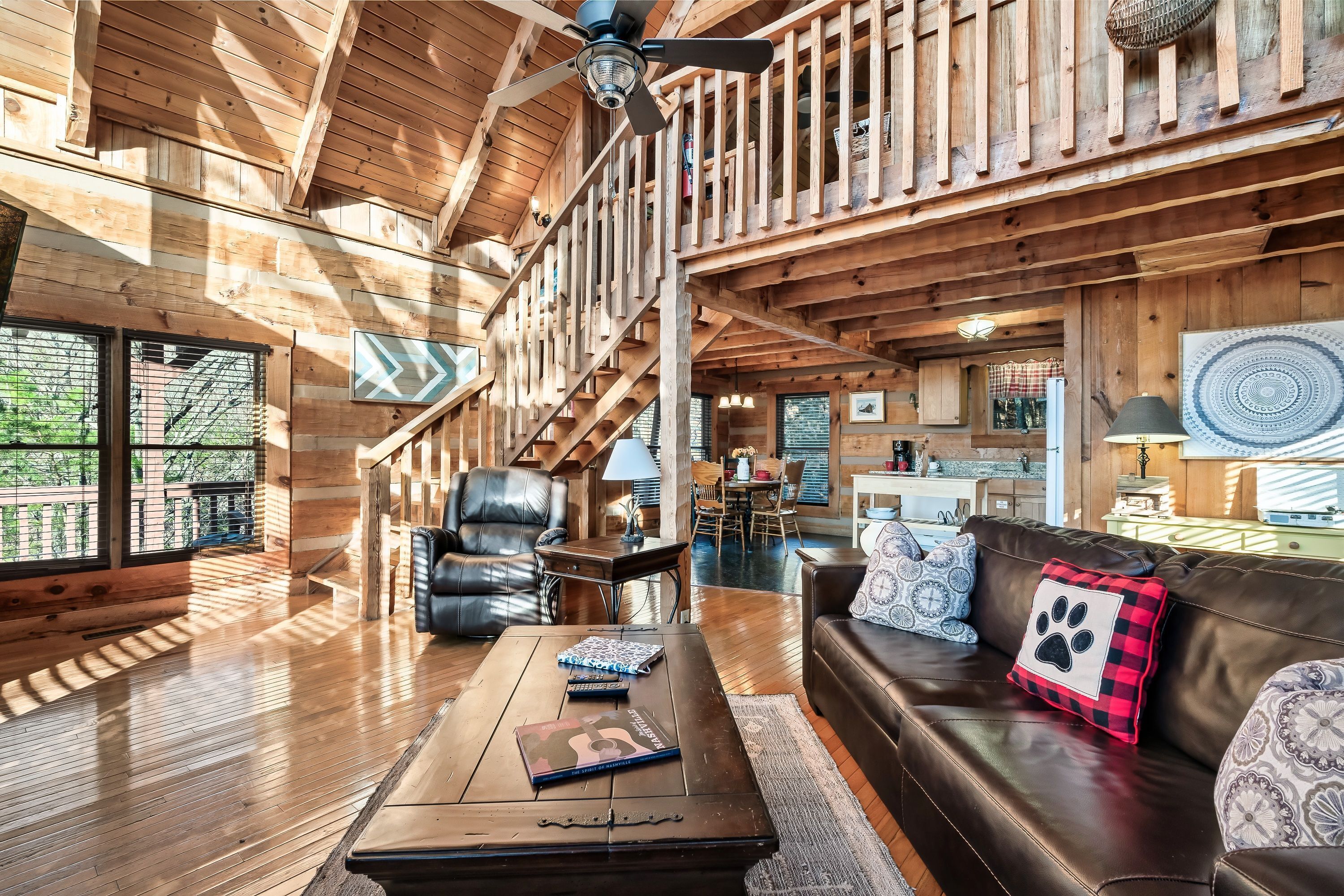 Ein geräumiger Holzraum mit hoher Decke, einer Treppe, einem Ledersofa und einem Couchtisch mit Büchern.