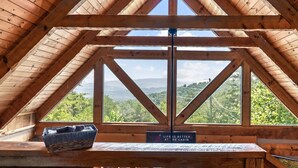 A wooden cabin with a sloped roof and large windows offering a view of a forested landscape.