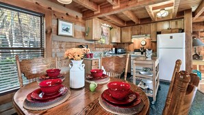 A wooden cabin interior with a dining table set with red bowls and plates, a white pitcher, and a green vase.