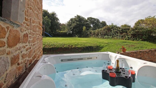 A hot tub with a stone wall and a grassy yard with trees. - Family house with enclosed garden and spa near the beach (Saint-Germain-le-Gaillard)