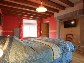 Un dormitorio con una cama grande, vigas de madera, un televisor y una pared de piedra.
