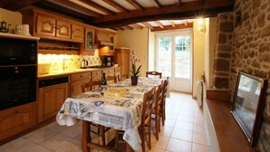 A kitchen with wooden cabinets, a dining table with a newspaper tablecloth, and a stone wall. - Family house with enclosed garden and spa near the beach (Saint-Germain-le-Gaillard)