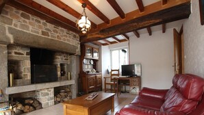 A cozy living room with a stone fireplace, wooden beams, a leather sofa, and a television. - Family house with enclosed garden and spa near the beach (Saint-Germain-le-Gaillard)