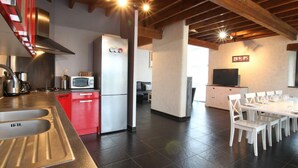 A modern kitchen with a stainless steel sink, red cabinets, and a built-in microwave. There is a dining area with white chairs and a table, and a TV mounted on the wall.