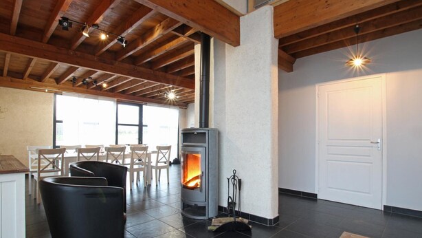 A cozy room with a fireplace, wooden beams, and a dining area with chairs.