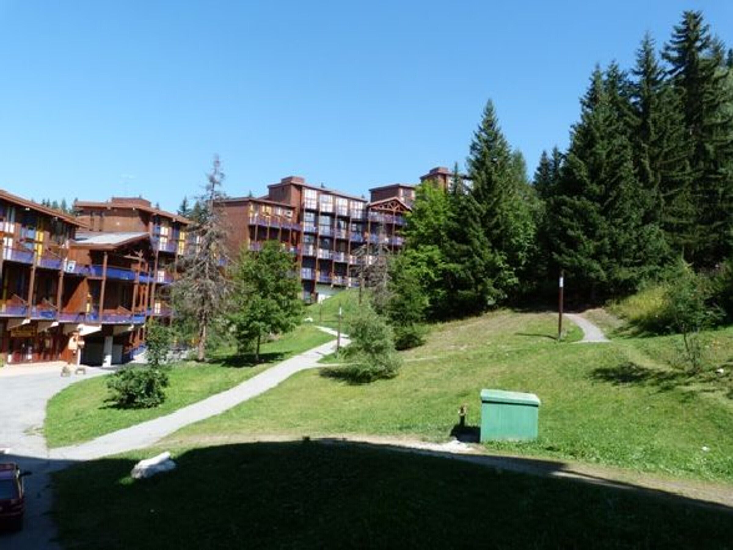 A multi-story hotel with balconies, surrounded by trees and a grassy area.