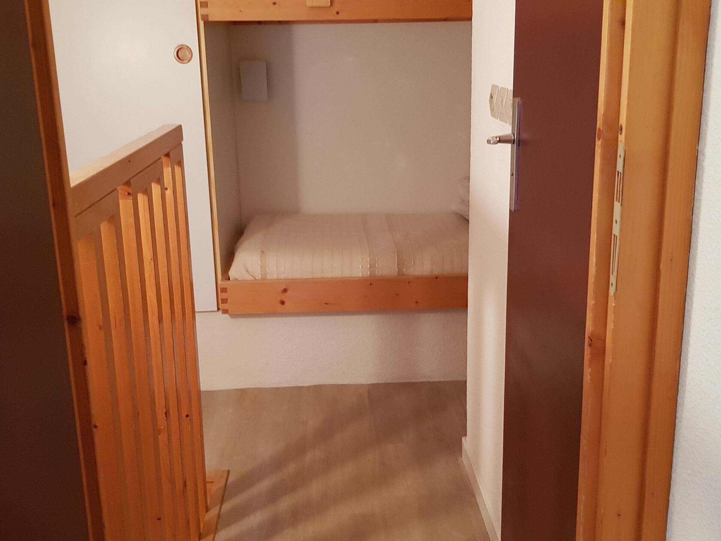 A narrow room with a bunk bed, a door, and a small window.