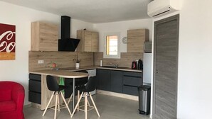 A compact kitchen with a central island, a red chair, a small trash bin, and a red stool. - Appartement LIMONE - 3*-  Plage à pied (FAVONE CONCA)