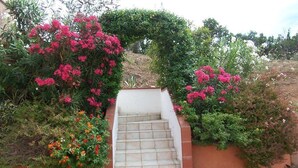 A set of outdoor stairs leading up to a white wall, surrounded by lush greenery and flowering plants. - Appartement LIMONE - 3*-  Plage à pied (FAVONE CONCA)