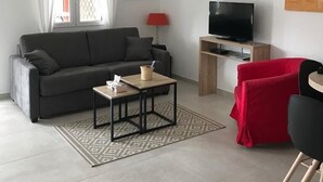 A modern living room with a grey sofa, a small coffee table, a red chair, a TV on a wooden stand, and a large Coca-Cola poster on the wall. - Appartement LIMONE - 3*-  Plage à pied (FAVONE CONCA)