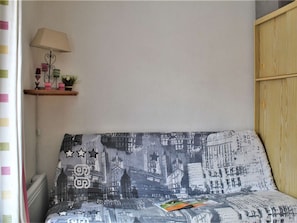 A bedroom with a cityscape bedspread, a bedside lamp, and a small shelf with decorative items.
