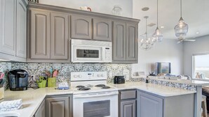 Une cuisine moderne avec des meubles gris, une cuisinière blanche et un four à micro-ondes. On y trouve des luminaires suspendus et une fenêtre donnant sur un beau paysage.