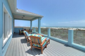 Une terrasse couverte, dotée de mobilier en bois et offrant une vue sur la plage.