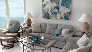 Un salon moderne avec vue sur l’océan, comprenant un canapé, des fauteuils, une table basse et deux lampes.
