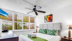 A bedroom with a bed, a desk, a ceiling fan, and a window with blinds.