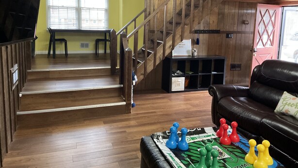 A wooden staircase leading to a second floor, a dining area with a table and chairs, and a living room with a leather couch and a board game. - Owl House, 5 bed 3 Bath - Game Room , Six Flags - Braves - Aquarium. (Mableton)