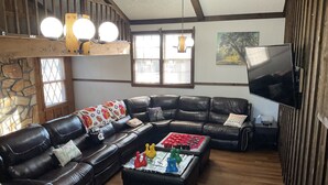 A cozy living room with a sectional sofa, a coffee table with board games, and a flat-screen TV. - Owl House, 5 bed 3 Bath - Game Room , Six Flags - Braves - Aquarium. (Mableton)
