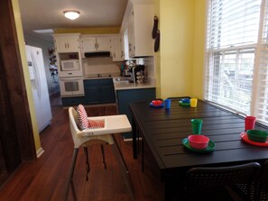 A kitchen with wooden cabinets, a dining table with colorful cups, and a high chair.