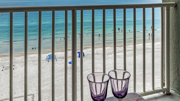 A balcony with a view of a beach, two empty wine glasses on a table, and a railing. - SUMMER SPECIAL Direct Beachfront!! MILLION View (Indian Shores)