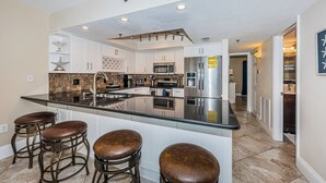 A modern kitchen with white cabinets, a large island with stools, stainless steel appliances, and a decorative star on the wall. - SUMMER SPECIAL Direct Beachfront!! MILLION View (Indian Shores)