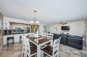 A modern kitchen with white cabinets, a dining table with chairs, and a black leather sofa in the living area.