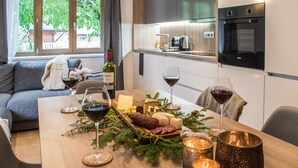 A modern kitchen with a dining table set for a meal, featuring a variety of cheeses, cured meats, and glasses of red wine. - Ipê - Modern | Sauna | Morzine (Montriond)