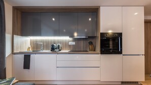 A modern kitchen with white cabinets, a built-in oven, and a countertop with a kettle and coffee maker. - Ipê - Modern | Sauna | Morzine (Montriond)