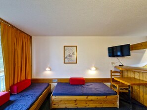 Una habitació amb dos llits de fusta, una banca vermella, una televisió penjada a la paret i un quadre.