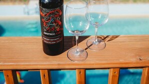 A bottle of Apothic Cabernet Sauvignon and two glasses on a wooden deck with a pool and ocean view in the background. - Riverfront*Shared Pool*3-Minute Walk to the Beach (202) (Brevard County)