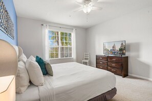Un dormitorio con cama, televisión, cómoda y ventana con cortinas.