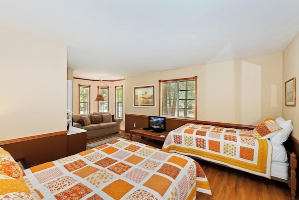 Habitación de hotel con dos camas, un sofá, un televisor y una ventana con persianas.