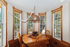Enjoy meals in this dining area with a wooden table and four chairs, surrounded by large windows and a woven pendant light.