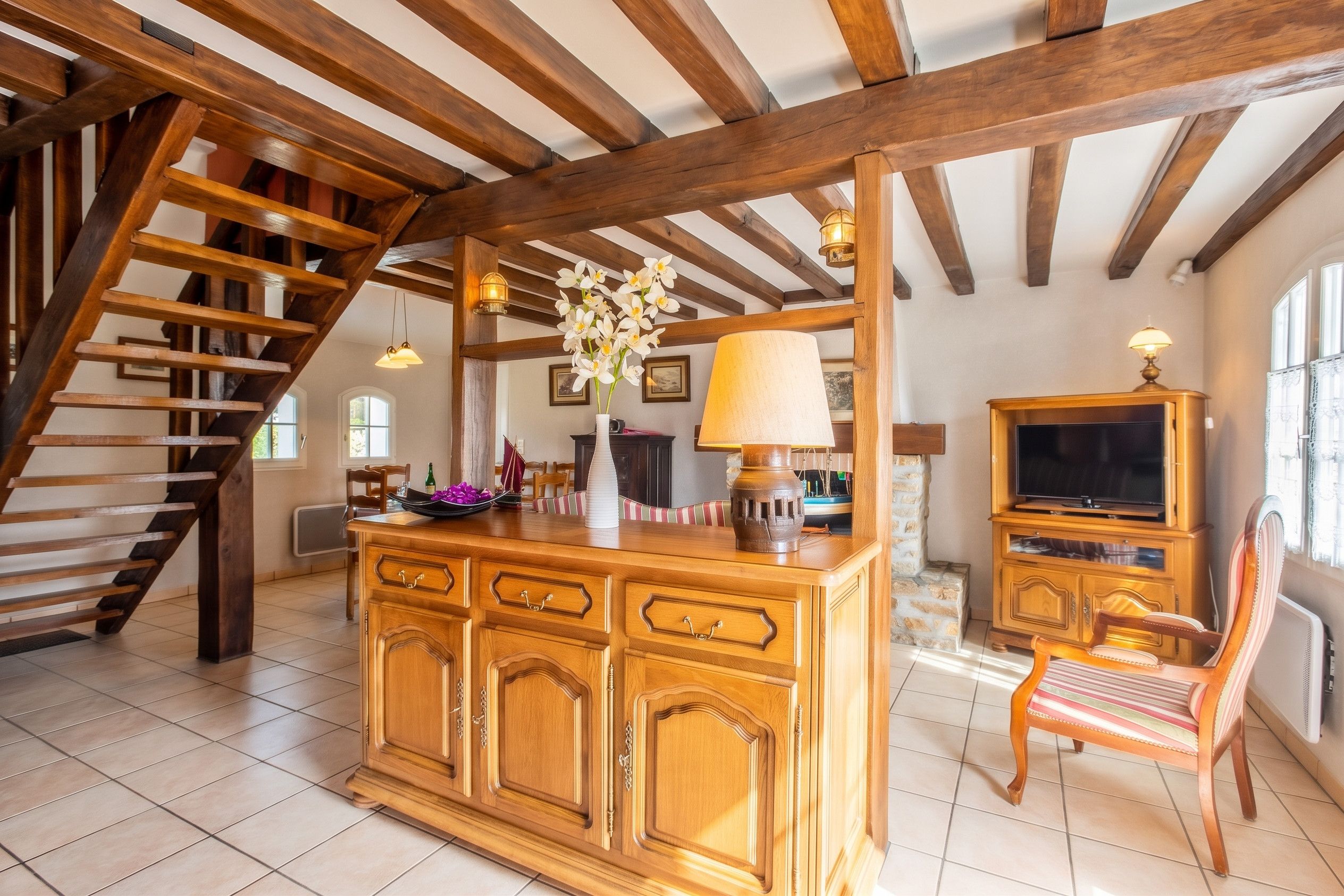 A spacious living area with a wooden staircase, a large wooden cabinet, a television, and a chair.