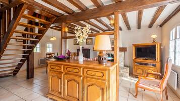 A spacious living area with a wooden staircase, a large wooden cabinet, a television, and a chair.