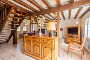 Un amplio salón con una escalera de madera, un mueble grande de madera, un televisor y una silla.