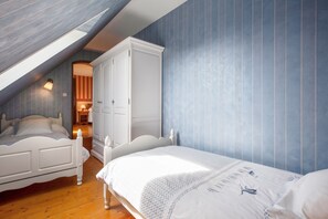 Un dormitorio con techo inclinado, dos camas, un armario y una pequeña zona de estar con una lámpara.
