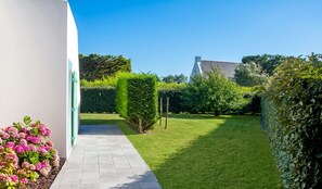 A well-maintained garden with a paved pathway leading to a grassy lawn, surrounded by neatly trimmed hedges and flowering plants.