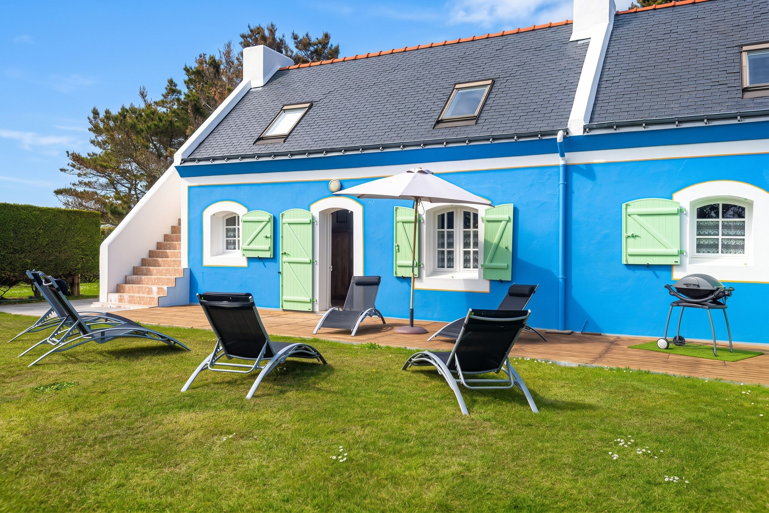 Een huis met een blauwe gevel, een grijs dak en een klein terras met tuinmeubilair.