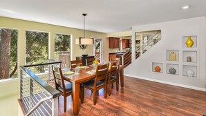 Un comedor amplio con una mesa y sillas de madera, una cocina al fondo y una escalera que sube a otro nivel.