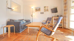 Una sala de estar con sofá, una mesa de madera, una mecedora, un televisor y una estantería.