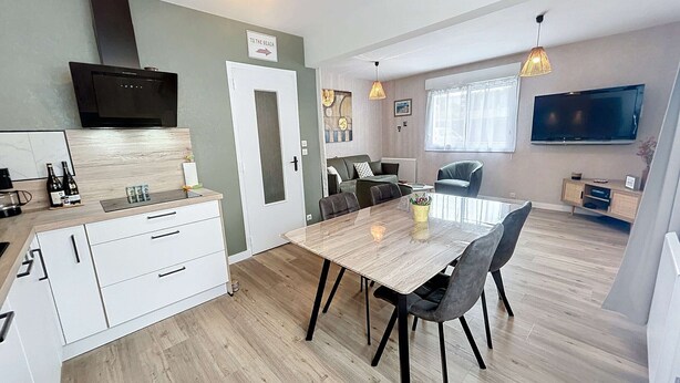 A modern apartment with a kitchen, dining area, and living room. It includes a flat-screen TV, a dining table with chairs, and a sofa. - Charming Renovated Apartment, Central Jullouville, 1 Bed, 4 Guests, Parking, 100m from Beach (Jullouville)